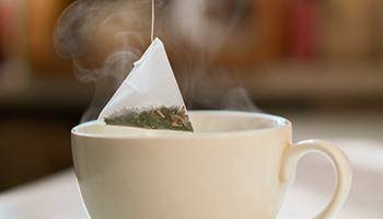 A person dipping a tea bag into a hot cup of water