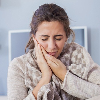Woman wearing sweater grasping cheek in pain