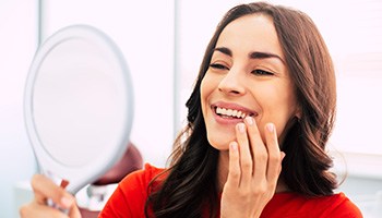 A woman admiring her restored smile with a hand mirror