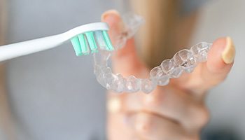 A patient using their toothbrush to clean an Invisalign tray