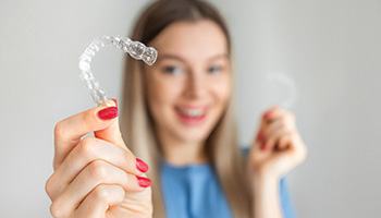 A blurred woman holding an Invisalign tray far from her face