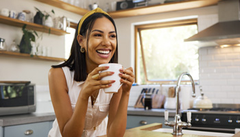 Woman smiling while drinking coffee in kitchen