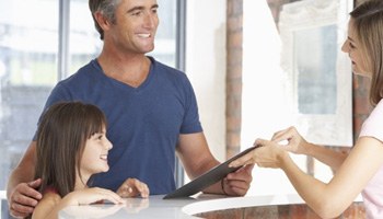 Father and daughter talking to a dental receptionist and smiling