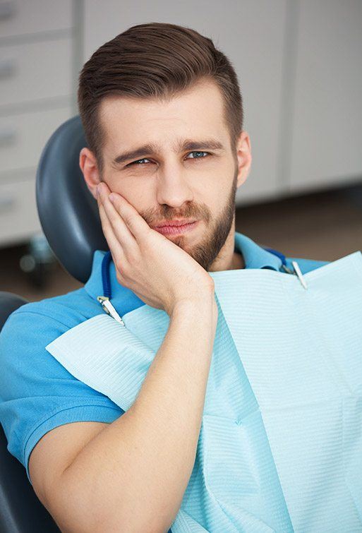 Man in teal polo holding cheek in pain