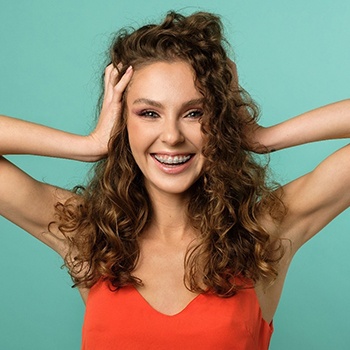 A young woman with curly hair smiling and showing off her metal braces after seeing a dentist in Metairie