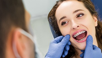 A dentist examining a female patient’s smile, complete with a full set of braces