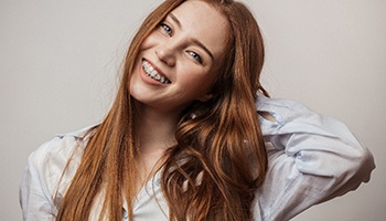 A young woman with long, red hair tilting her head to the side and smiling with a full set of braces in her mouth