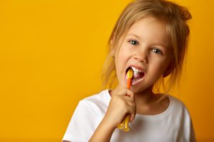 little girl brushing her teeth against yellow-orange background 
